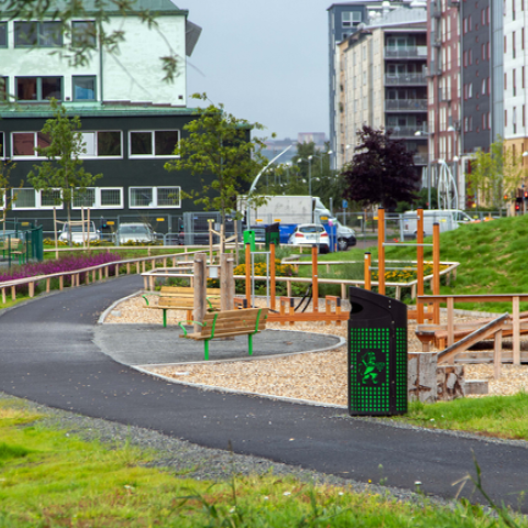 A picture of the new outdoor gym and a walking path through the park. Around it, green areas have different heights to lead rain water, and young trees have been planted.